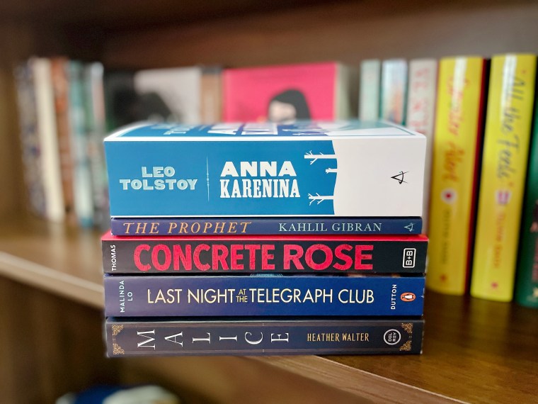 Photo shows a stack of books placed on a bookshelf. From top to bottom: Anna Karenina by Leo Tolstoy, The Prophet by Khalil Gibran, Concrete Rose by Angie Thomas, Last Night at the Telegraph Club by Malinda Lo, Malice by Heather Walter