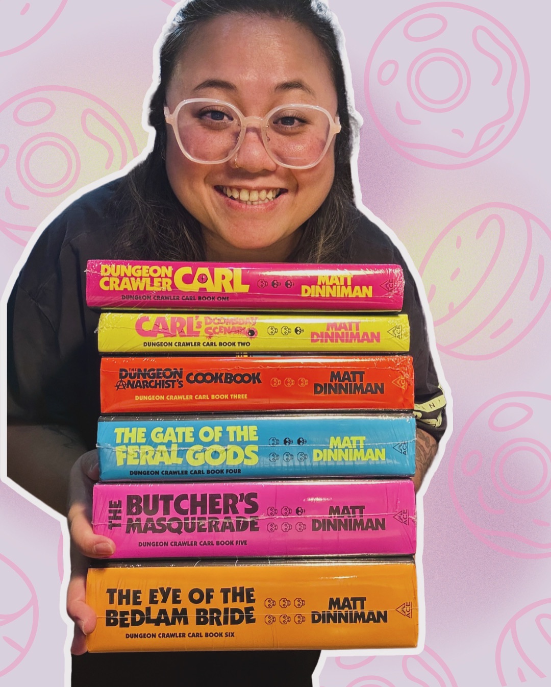 An image of a person holding a stack of six books from the Dungeon Crawler Carl series by Matt Dinniman. Edited in the background are outlines of donuts (referencing a character in the book).